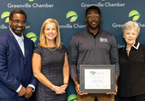 Group posing with a framed award in front of a Greenville Chamber backdrop