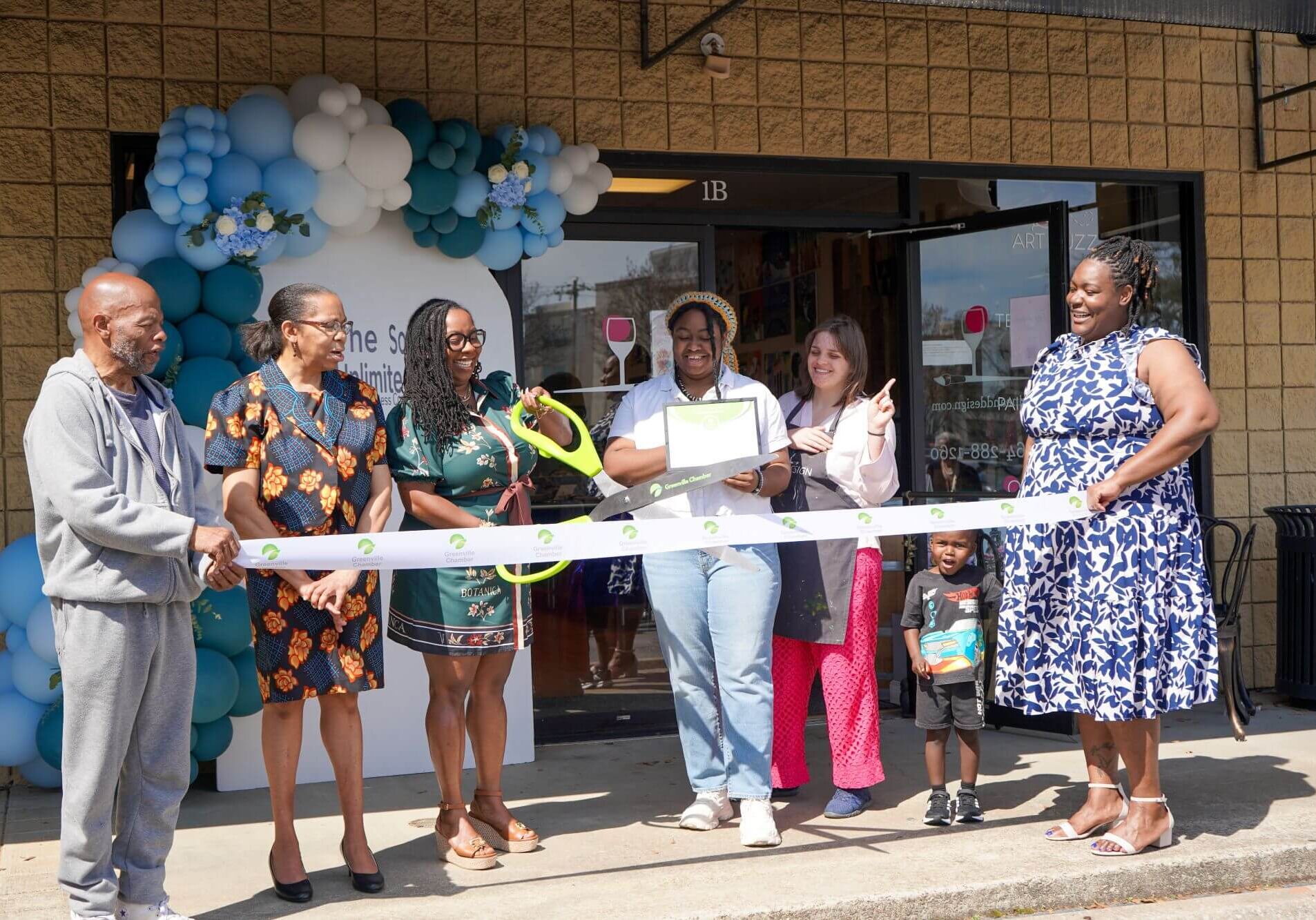 Ribbon cutting celebration outside a storefront decorated with balloons