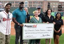 Group presenting an oversized Power:Ed check on a baseball field